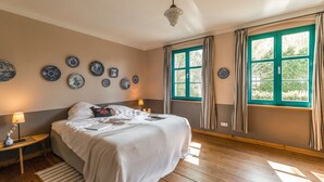 Un dormitorio con cama, mesitas de noche, platos en la pared y una ventana con cortinas.