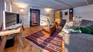 A cozy living room with a wooden floor, a television, a sofa, a patterned rug, and a vintage suitcase.