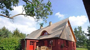 A red barn with a thatched roof, a wooden bench, and a grassy yard.