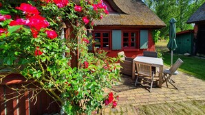 A house with a thatched roof, red walls, and a garden with red flowers.