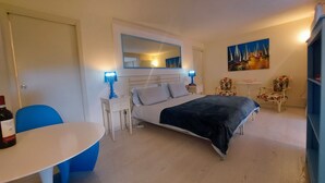 A bedroom with a bed, bedside tables, a chair, a small table, and a painting on the wall. - Lake Garda luxury studio with pool (Torri del Benaco)