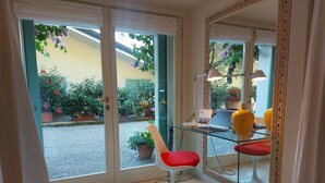 A room with a glass door leading to a garden, a desk with a laptop, a chair, and a large mirror. - Lake Garda luxury studio with pool (Torri del Benaco)