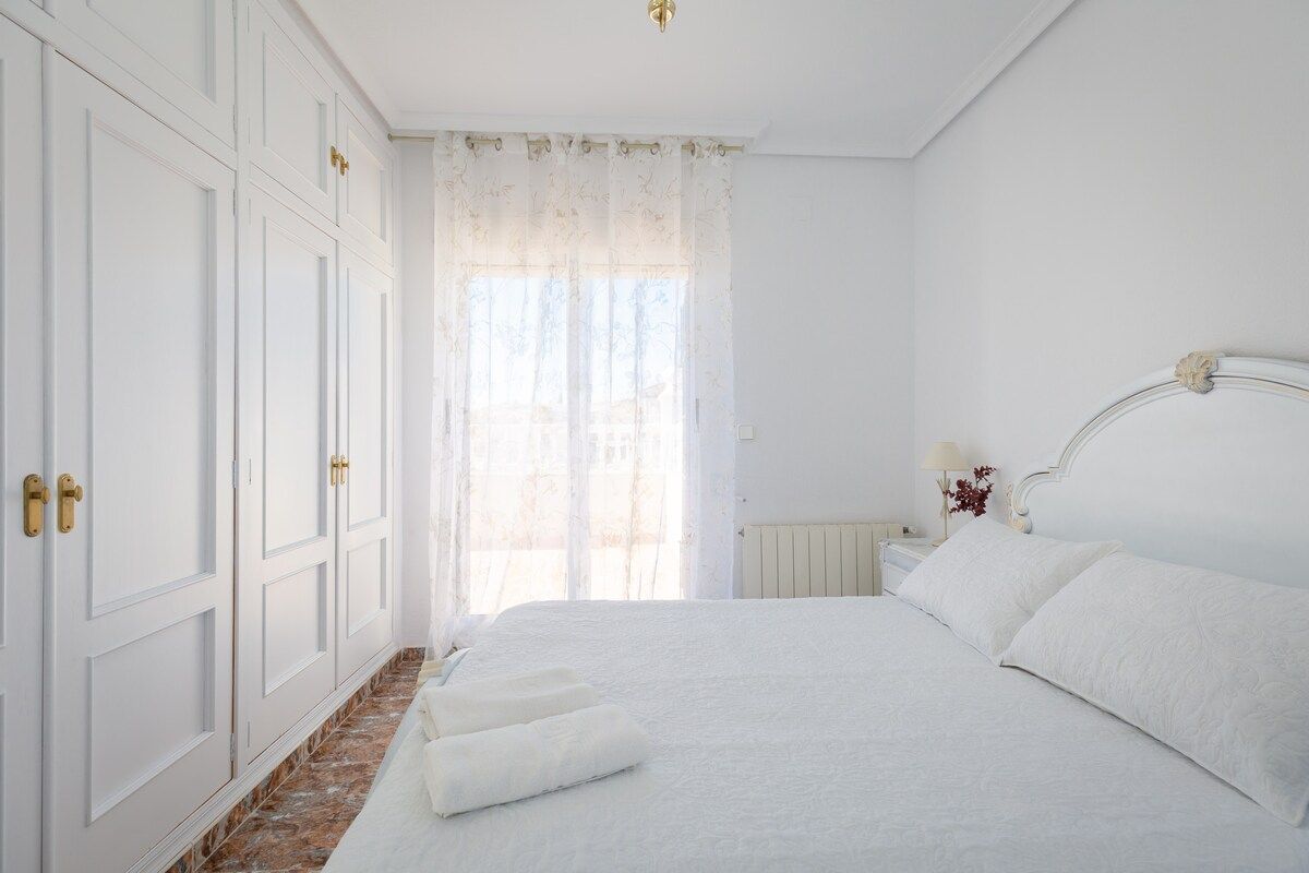 Une chambre à coucher avec un grand lit, des rideaux blancs et un radiateur.