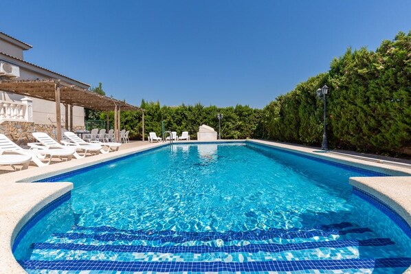 Ein Pool mit Liegestühlen und einer Pergola, umgeben von Grünpflanzen.