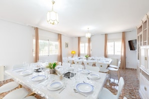 A dining area with tables set for a meal, featuring white chairs and a chandelier.