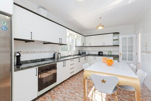 A modern kitchen with white cabinets, a built-in oven, a microwave, and a dining area with a white table and chairs. - Fidalsa Grand White House (Mutxamel / Muchamiel)