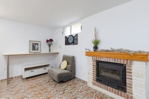 A living room with a fireplace, a chair, a shelf with a picture frame, and a dartboard. - Fidalsa Grand White House (Mutxamel / Muchamiel)