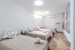 A hotel room with three beds, a window, an air conditioning unit, and a poster on the wall.