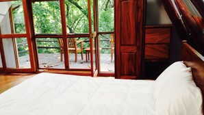 Quarto com uma cama grande, mobiliário de madeira e vista para o exterior através de portas de vidro.
