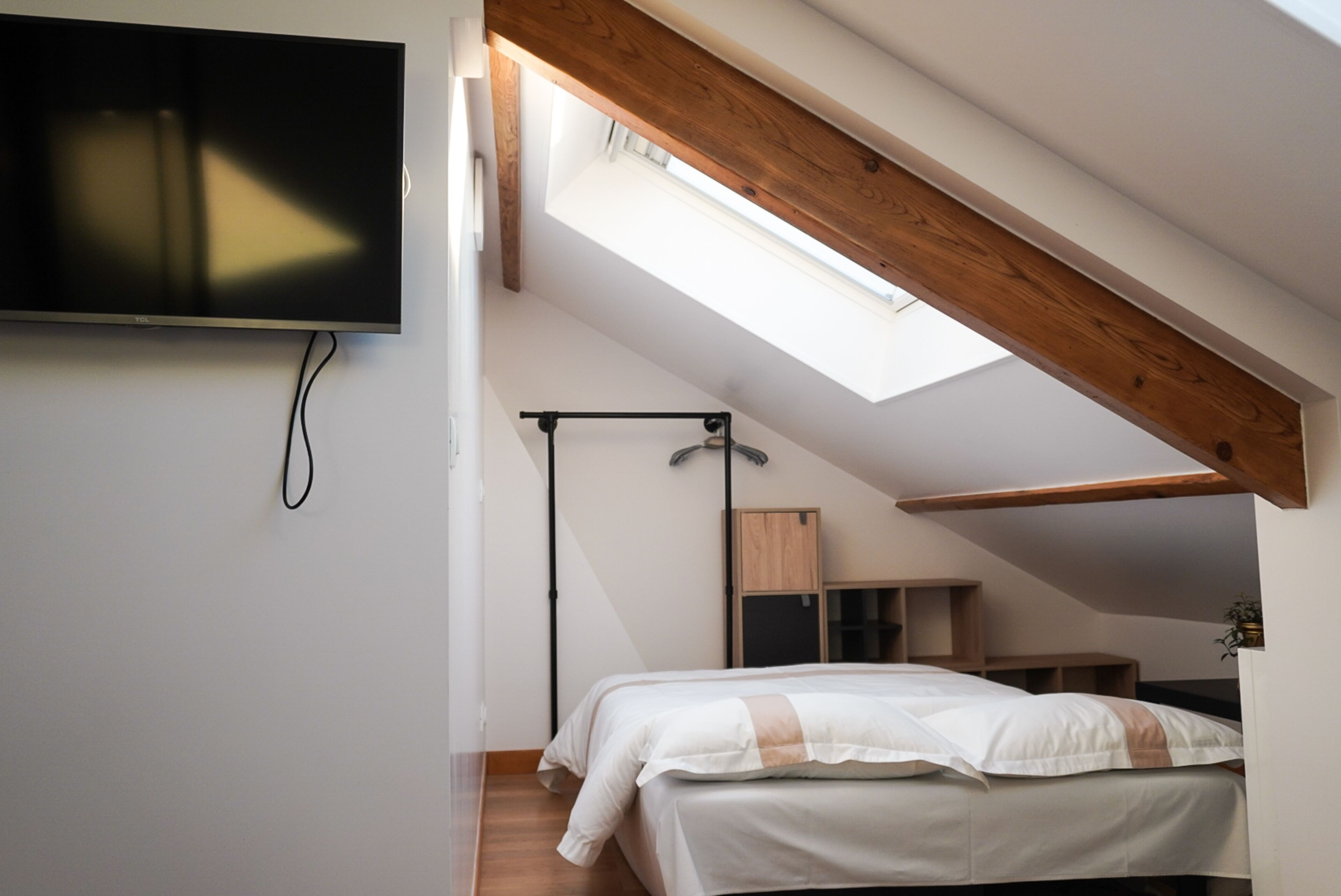 A bedroom with a skylight, a bed, a TV, and a wooden ceiling.