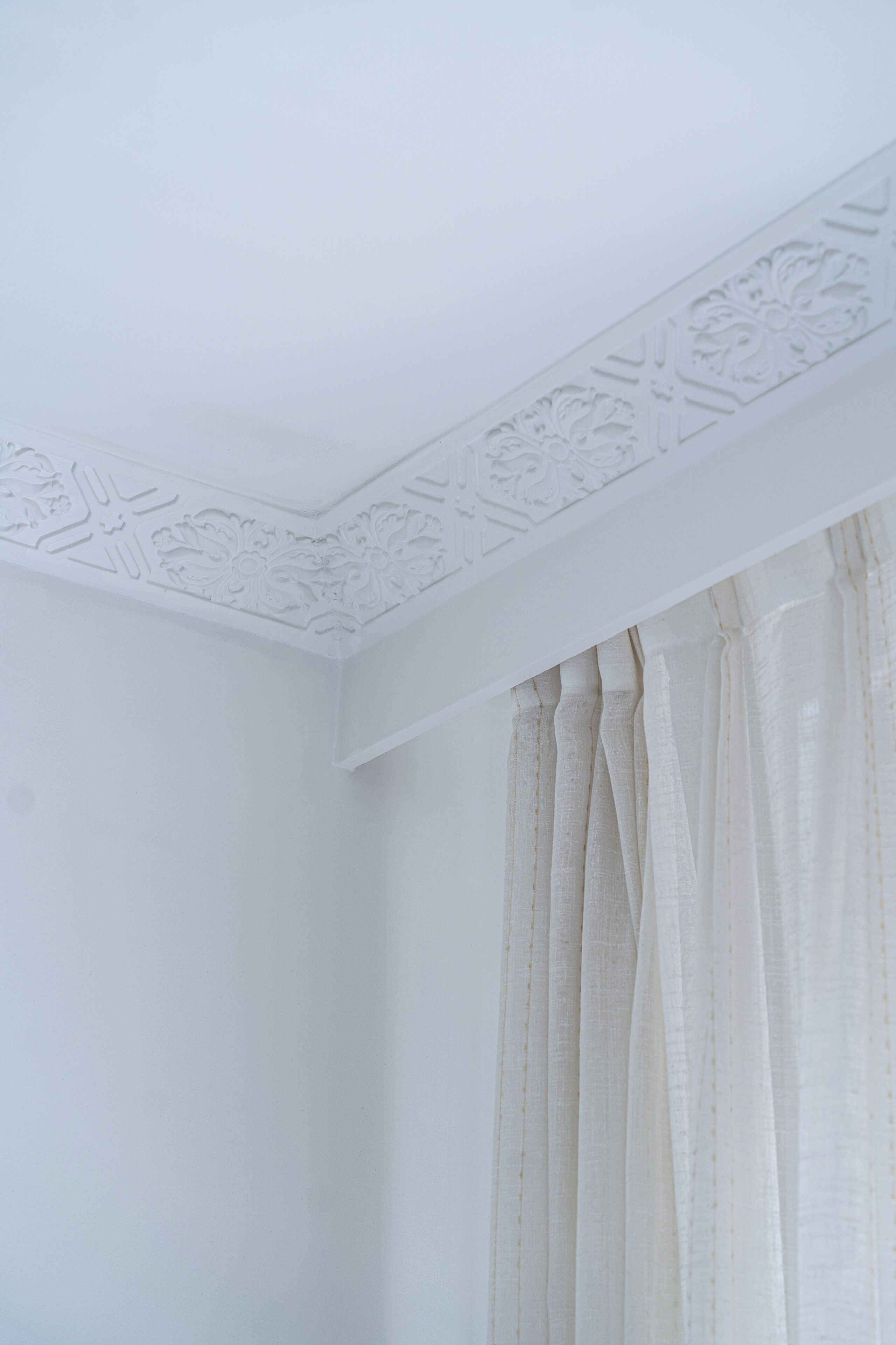 Esquina de una habitación con paredes y techo blancos, con molduras decorativas.