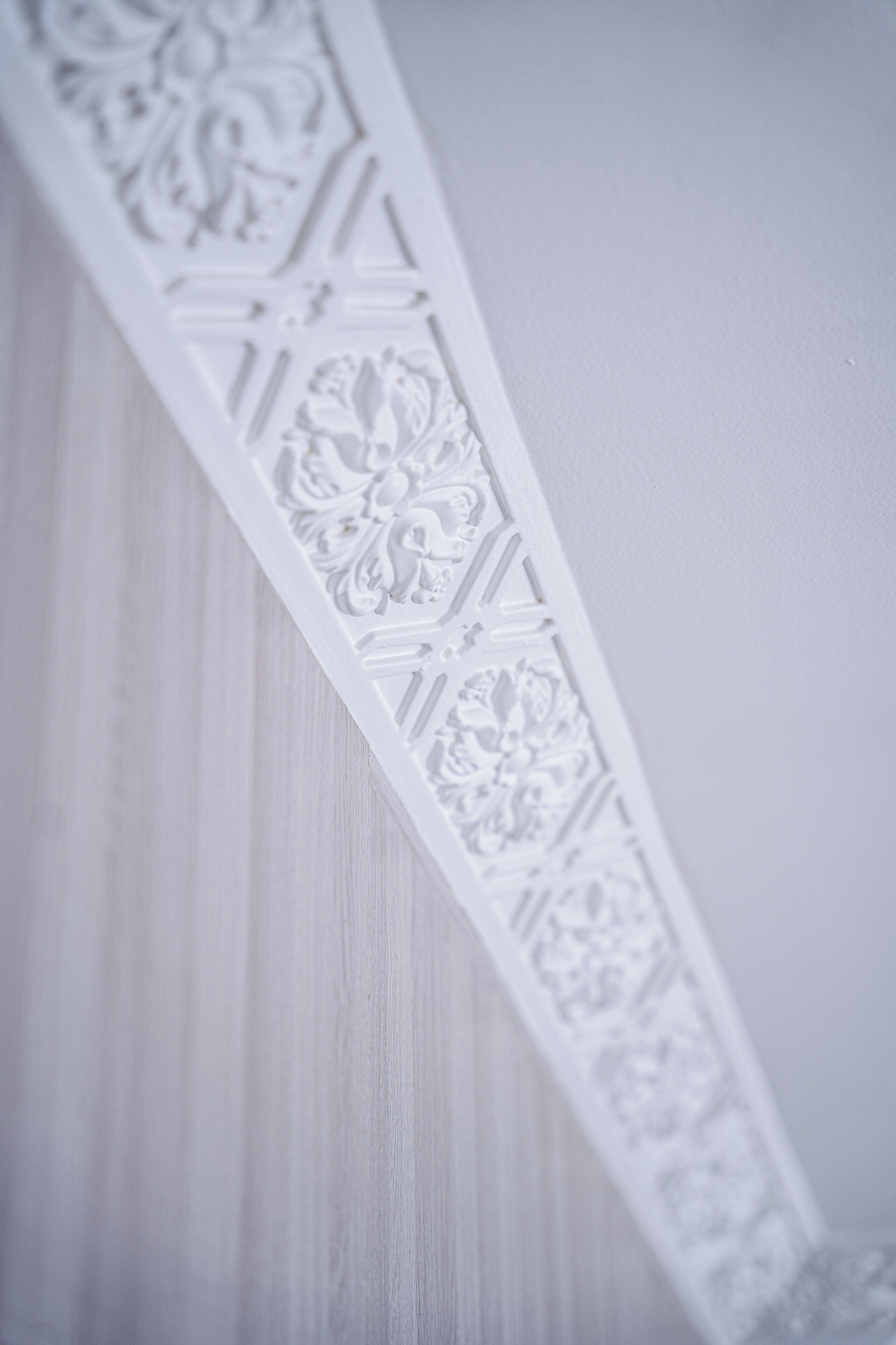 Un panneau en bois sculpté de motifs géométriques et floraux, peint en blanc et doté de détails complexes.