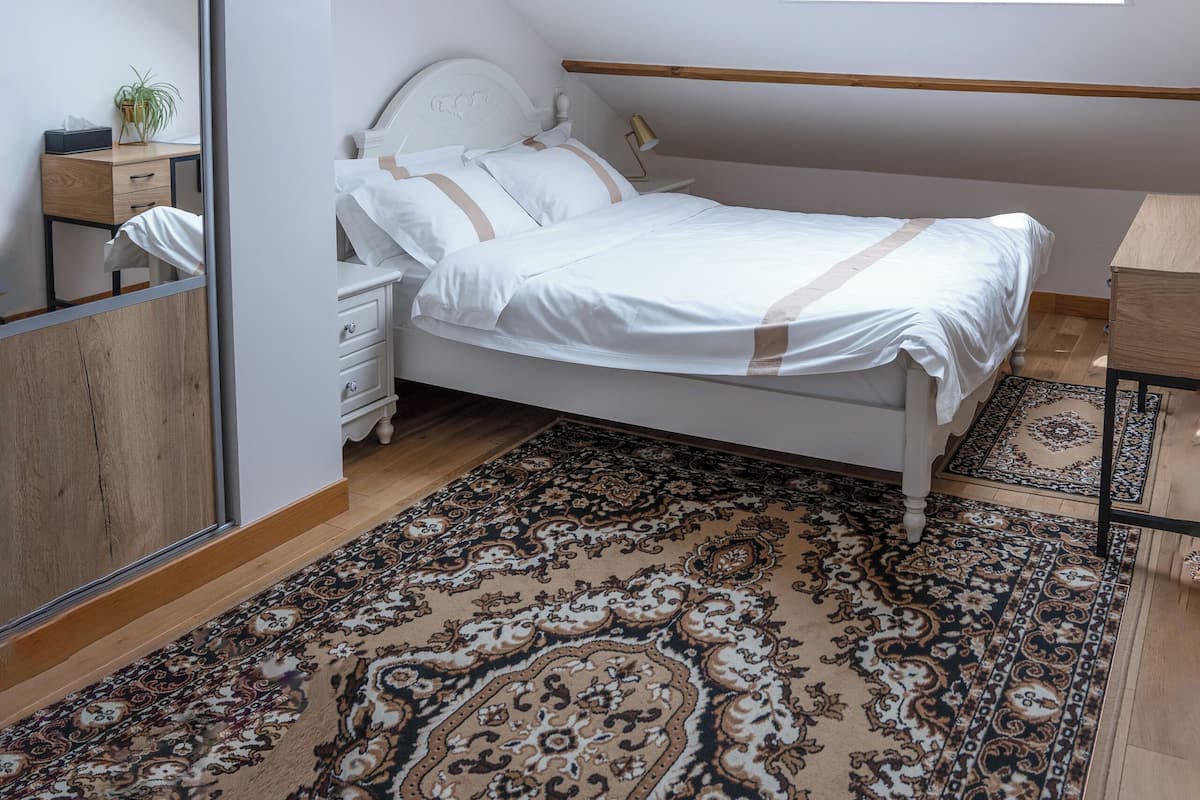 Une chambre à coucher avec un puits de lumière, un lit, une table de chevet, un miroir et un tapis à motifs.