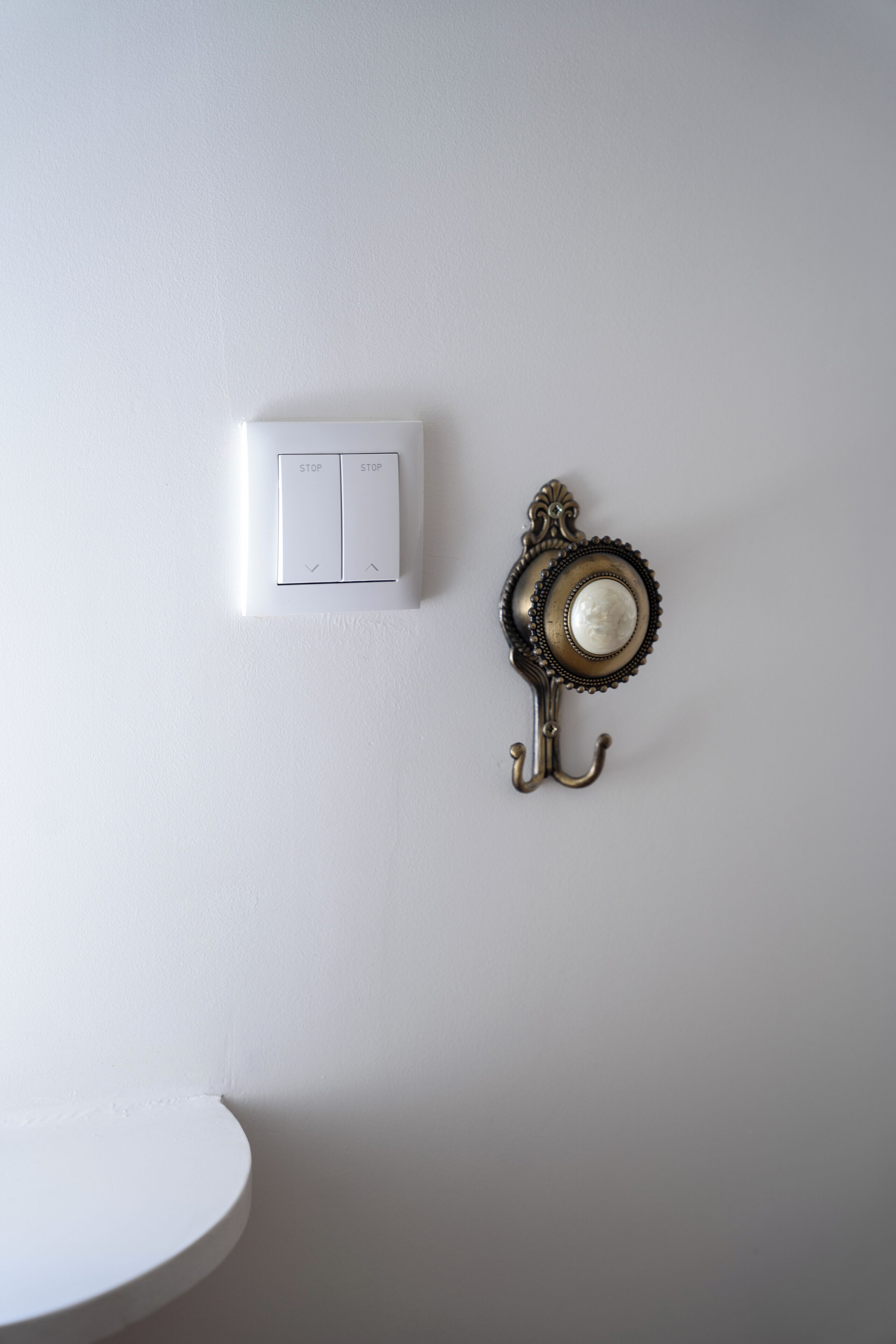 A white wall with a white switch and a decorative metal hook.