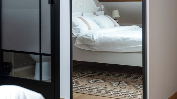 A bedroom with a large mirror, a bed with white linens, a wooden headboard, and a patterned rug. - La Maison Charentonneau (Maisons-Alfort)