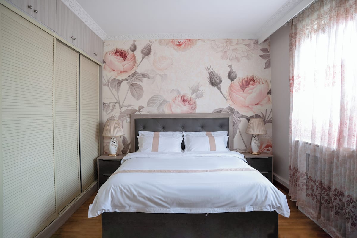 Une chambre à coucher avec un grand lit, deux tables de chevet avec des lampes, un papier peint à motifs floraux et une porte coulissante.