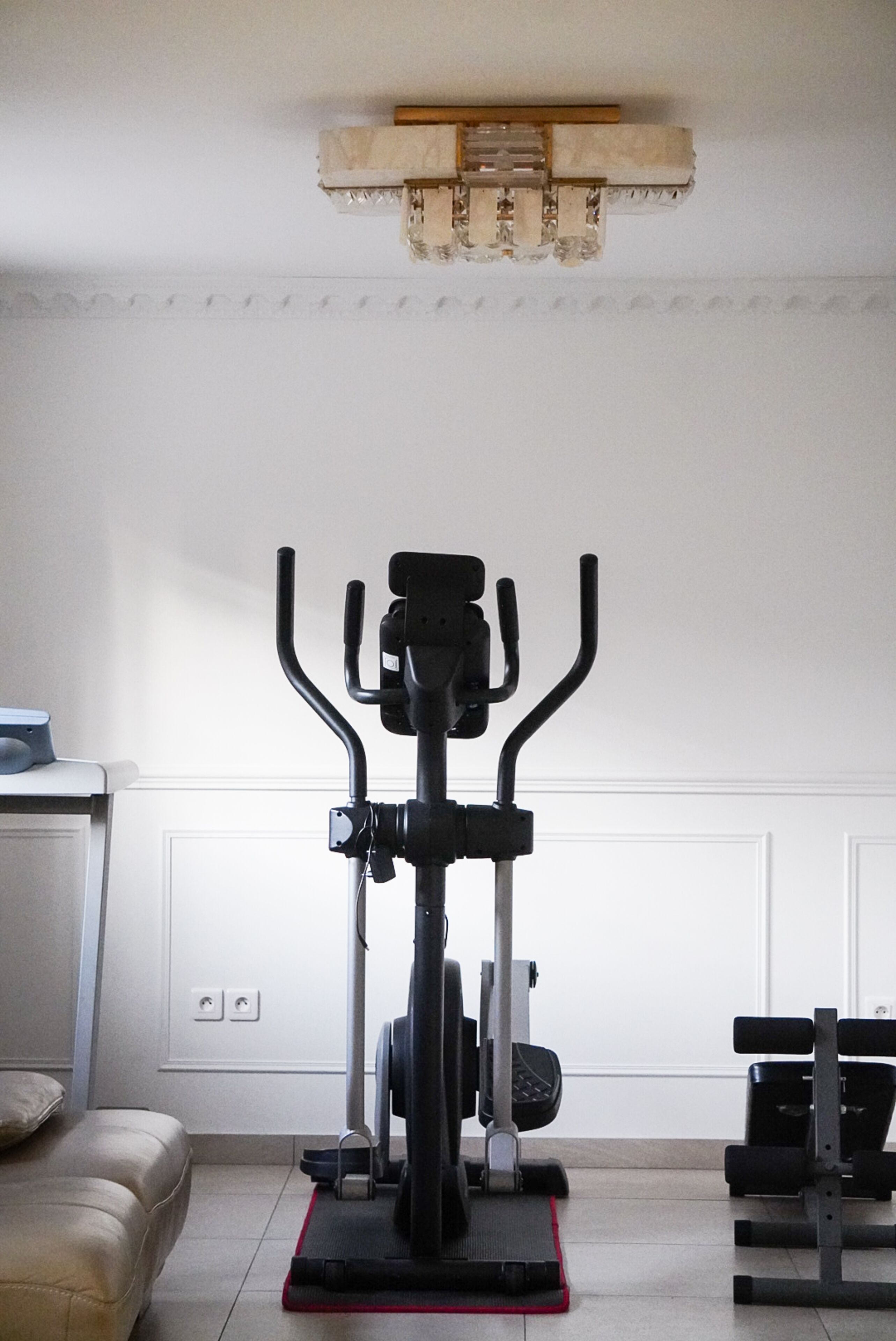 A home gym with an elliptical machine, a bench, and a small table with a laptop.