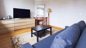 A living room with a sofa, a TV, a fireplace, and a chandelier. - La Maison Charentonneau (Maisons-Alfort)