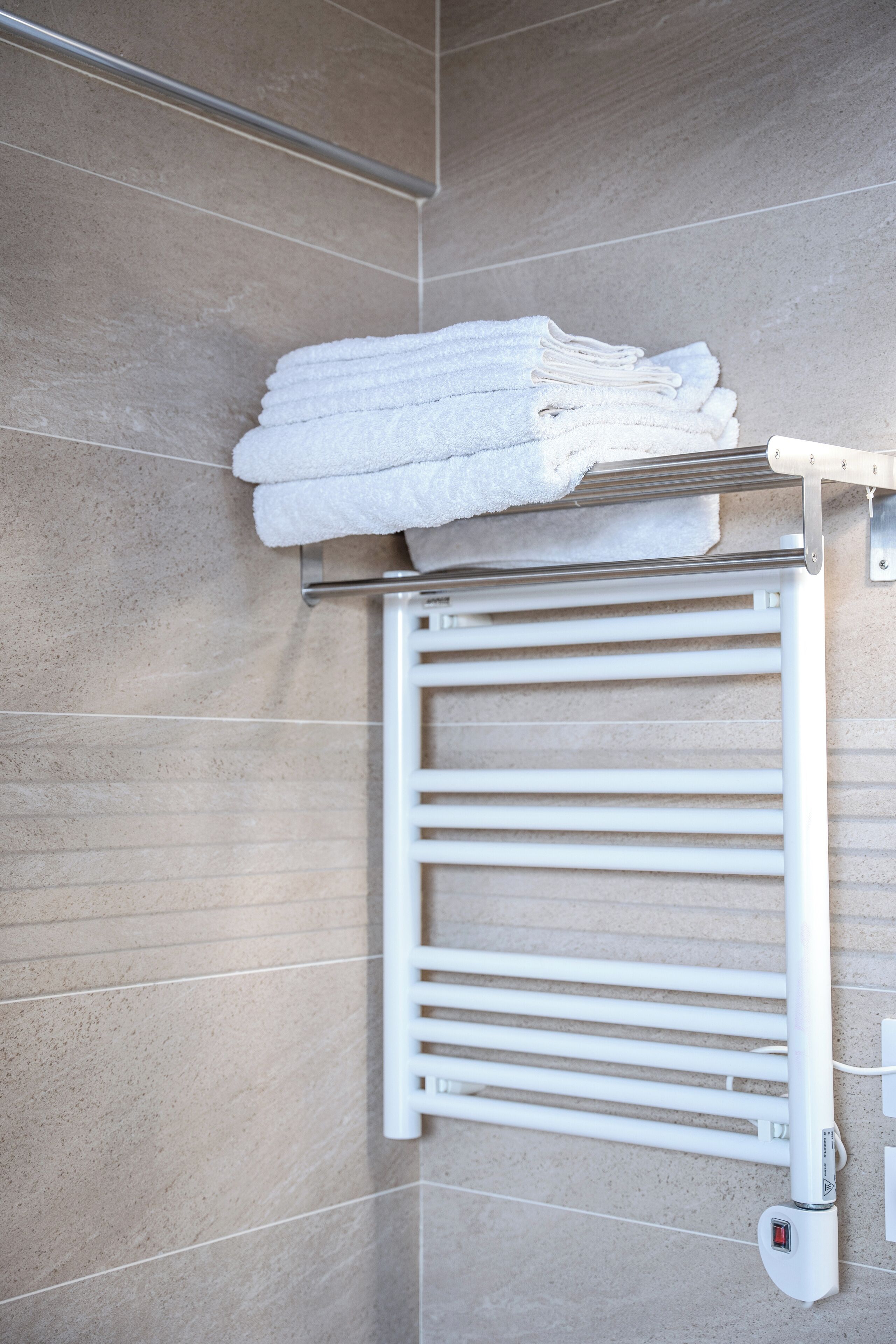 A bathroom with a towel rack holding folded towels, a white towel warmer, and a control panel.