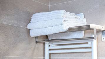 A bathroom with a towel rack holding folded towels, a white towel warmer, and a control panel.