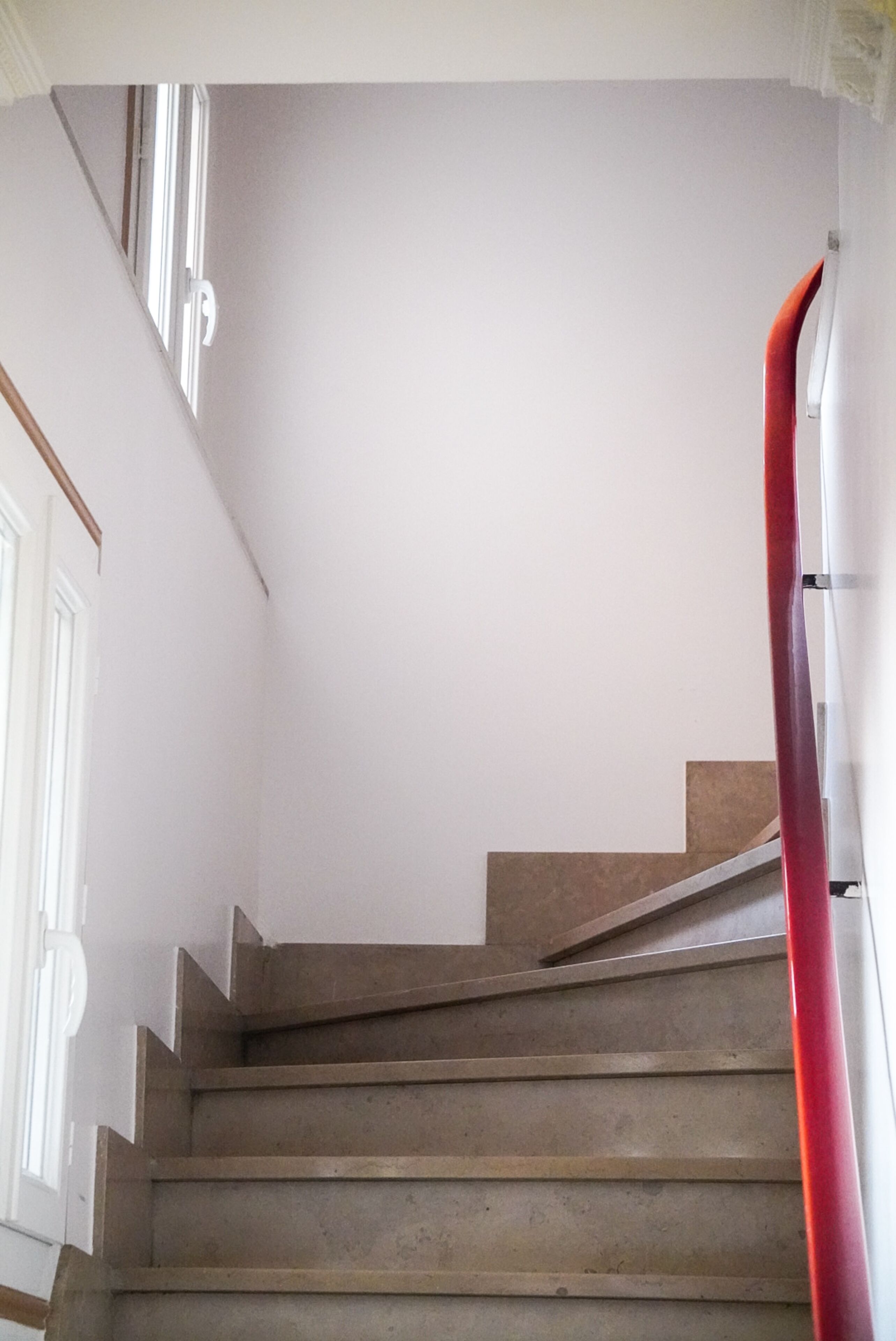 A staircase with a plain wall and a red handrail.