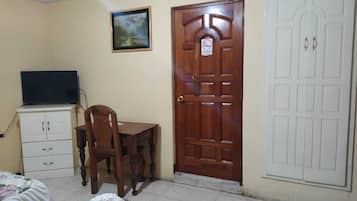 A bedroom with a bed, a wooden desk, a chair, a television on a cabinet, and two doors.