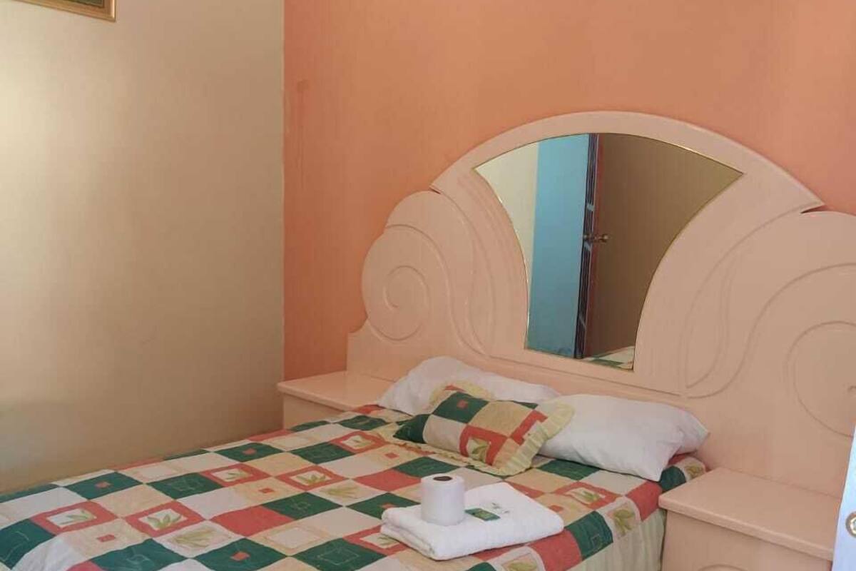A bedroom with a bed, a nightstand, a mirror, and a picture on the wall.