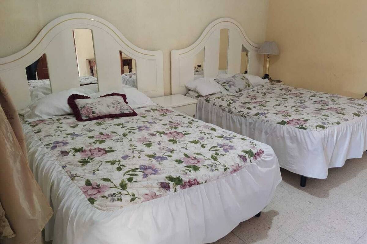 A hotel room with two beds, each with a floral bedspread and white headboards.