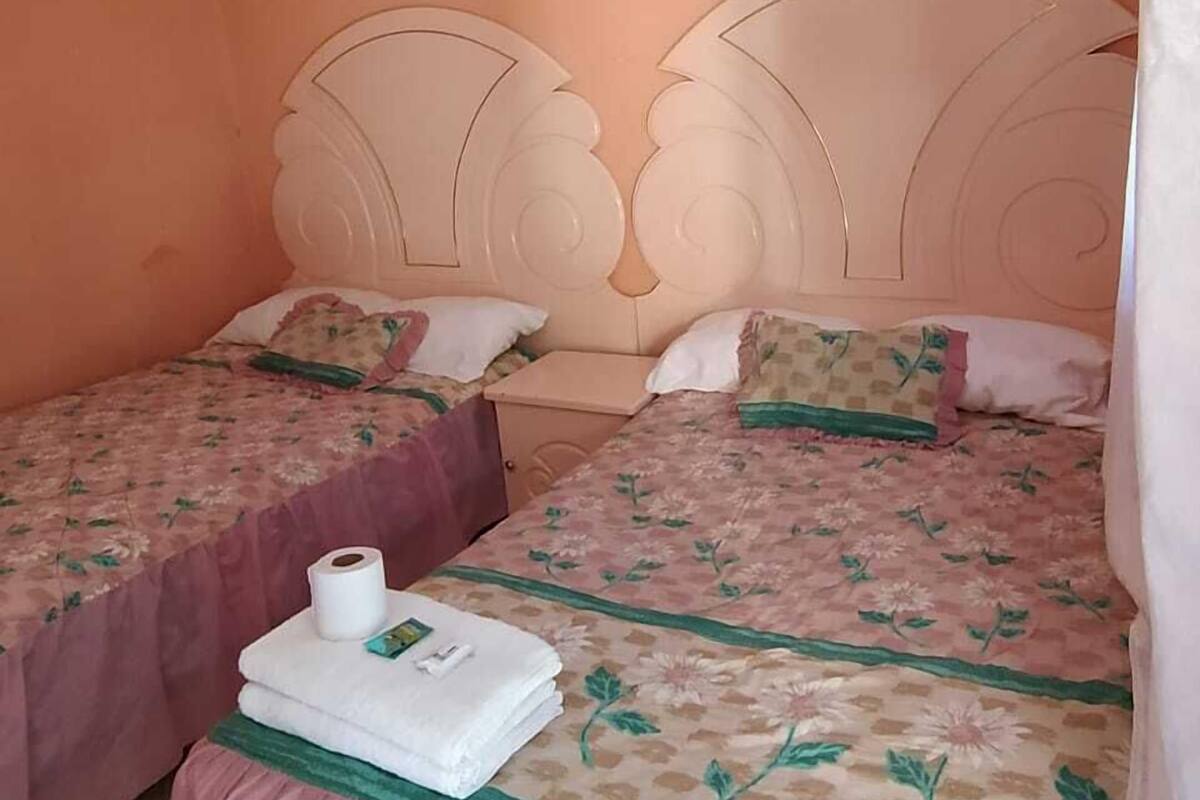 A room with two beds, each with a floral bedspread and matching pillows. There is a stack of white towels and a box on the floor.