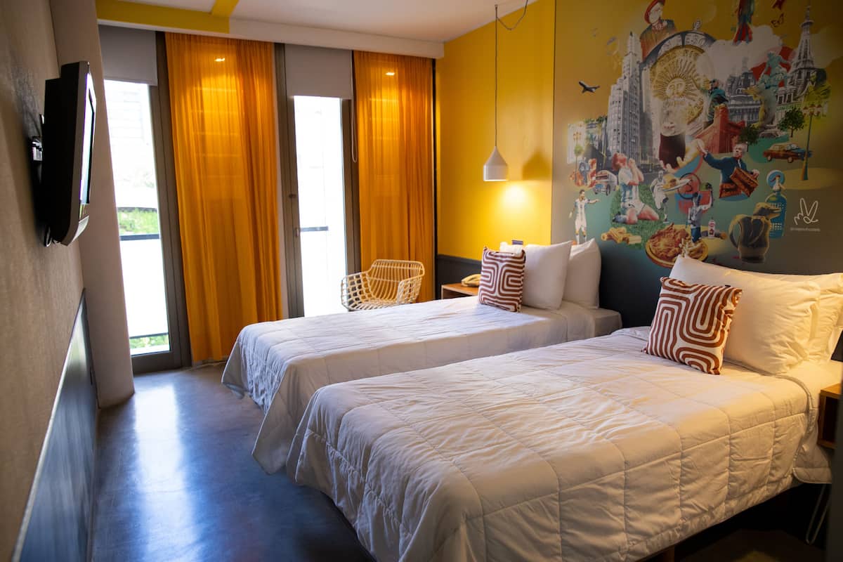 Habitación de hotel con dos camas, un televisor, una silla y un mural en la pared.