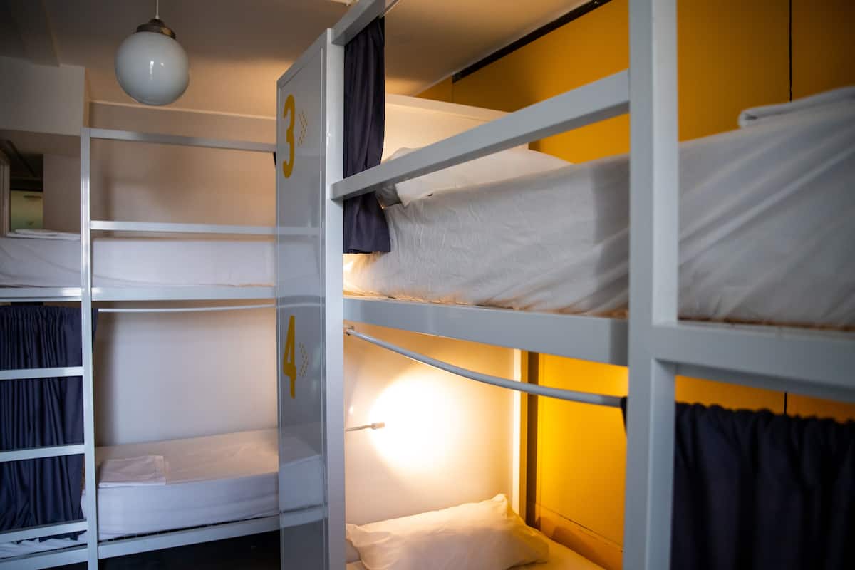 Dormitorio con literas, barandillas blancas y una única lámpara colgante.