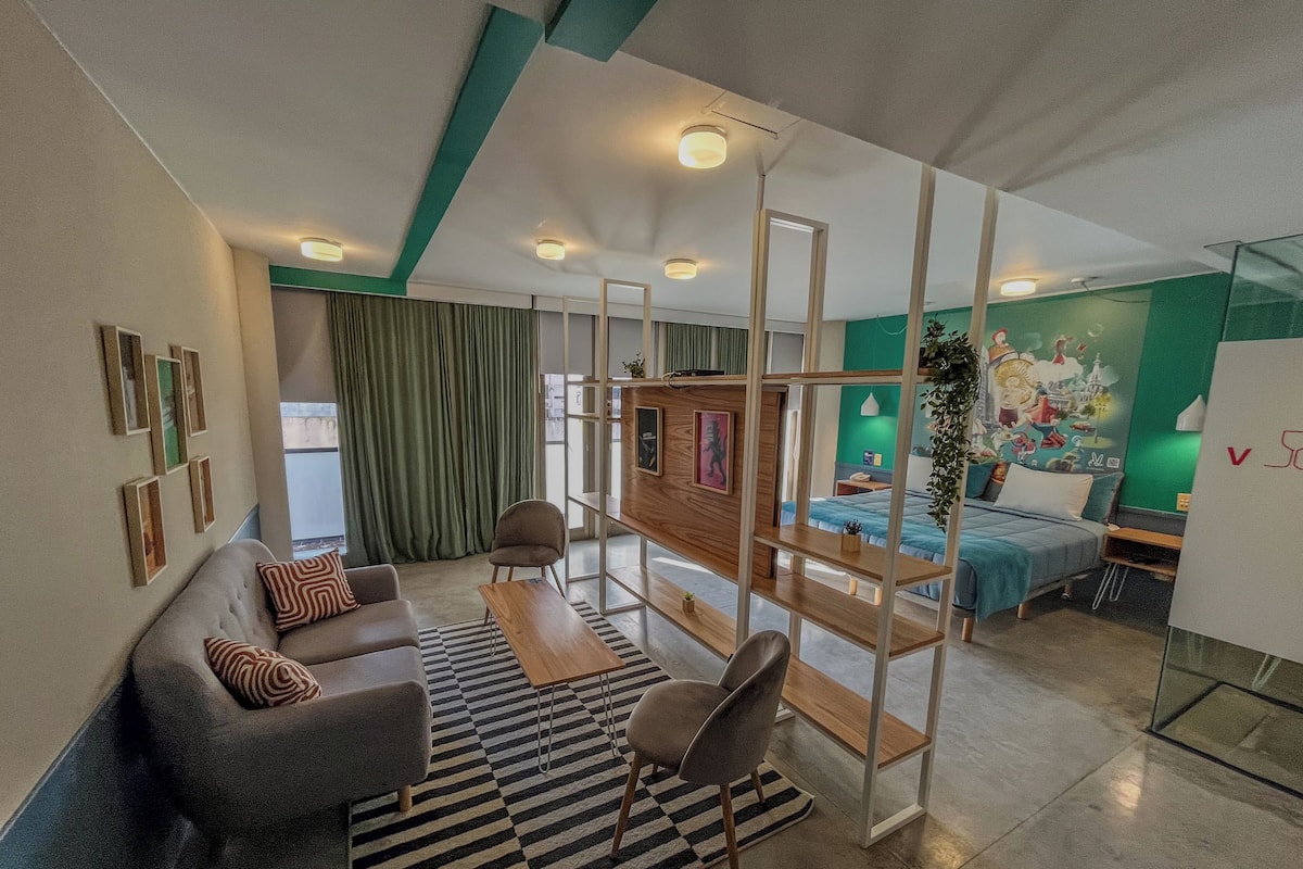 Una sala moderna con sofá, sillas, una mesita de centro y televisor. Se ve una cama con pared verde y un mural al fondo.