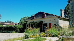 Ein Steinhaus mit Ziegeldach, einer roten Tür und einem Garten mit gelben Blumen.