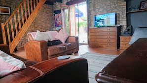 Ein gemütliches Wohnzimmer mit Steinwand, einer Holztreppe, einem Ledersofa, einem Fernseher und einer Holzkommode.