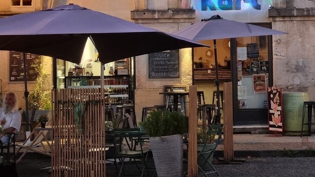 Ein Außenbereich mit Tischen und Stühlen vor einem Gebäude, an dem ein Schild mit dem Schriftzug 'Kurt' angebracht ist.