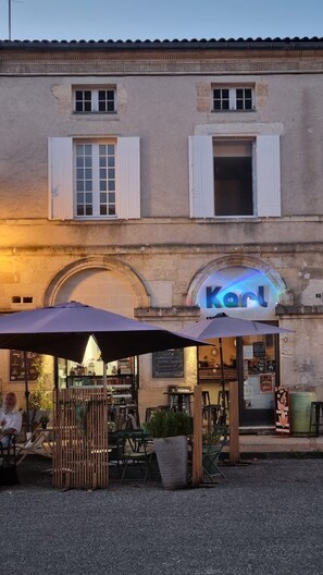 Un espace extérieur aménagé avec des tables et des chaises, situé devant un bâtiment sur lequel on peut lire l’inscription « Kurt ».