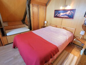 Ein gemütliches Zimmer mit einem Bett, einer Bank, einem Nachttisch und einem Bild an der Wand.