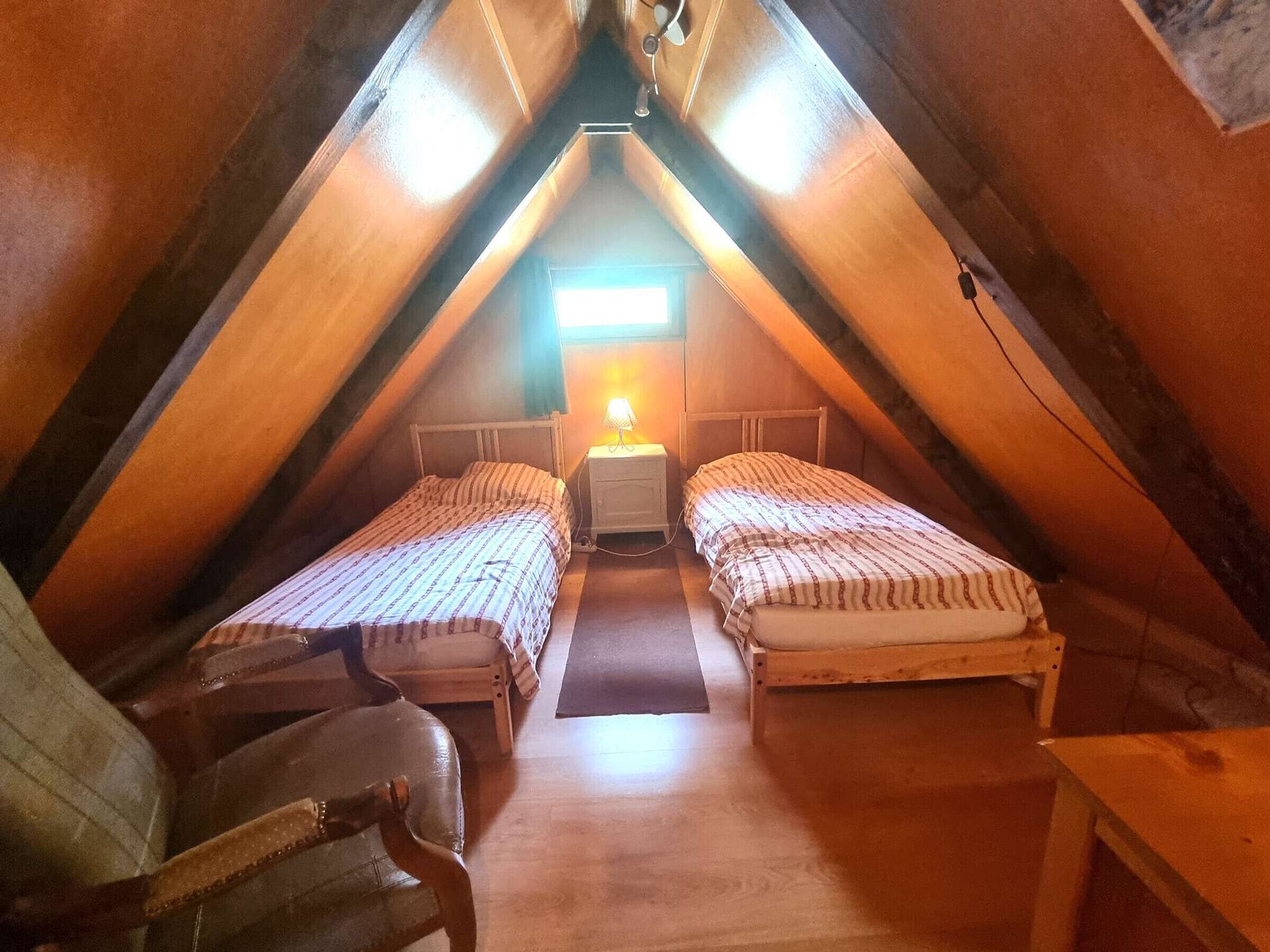 Ein kleines, gemütliches Schlafzimmer im Dachgeschoss mit zwei Einzelbetten, einem Nachttisch und einem Stuhl.