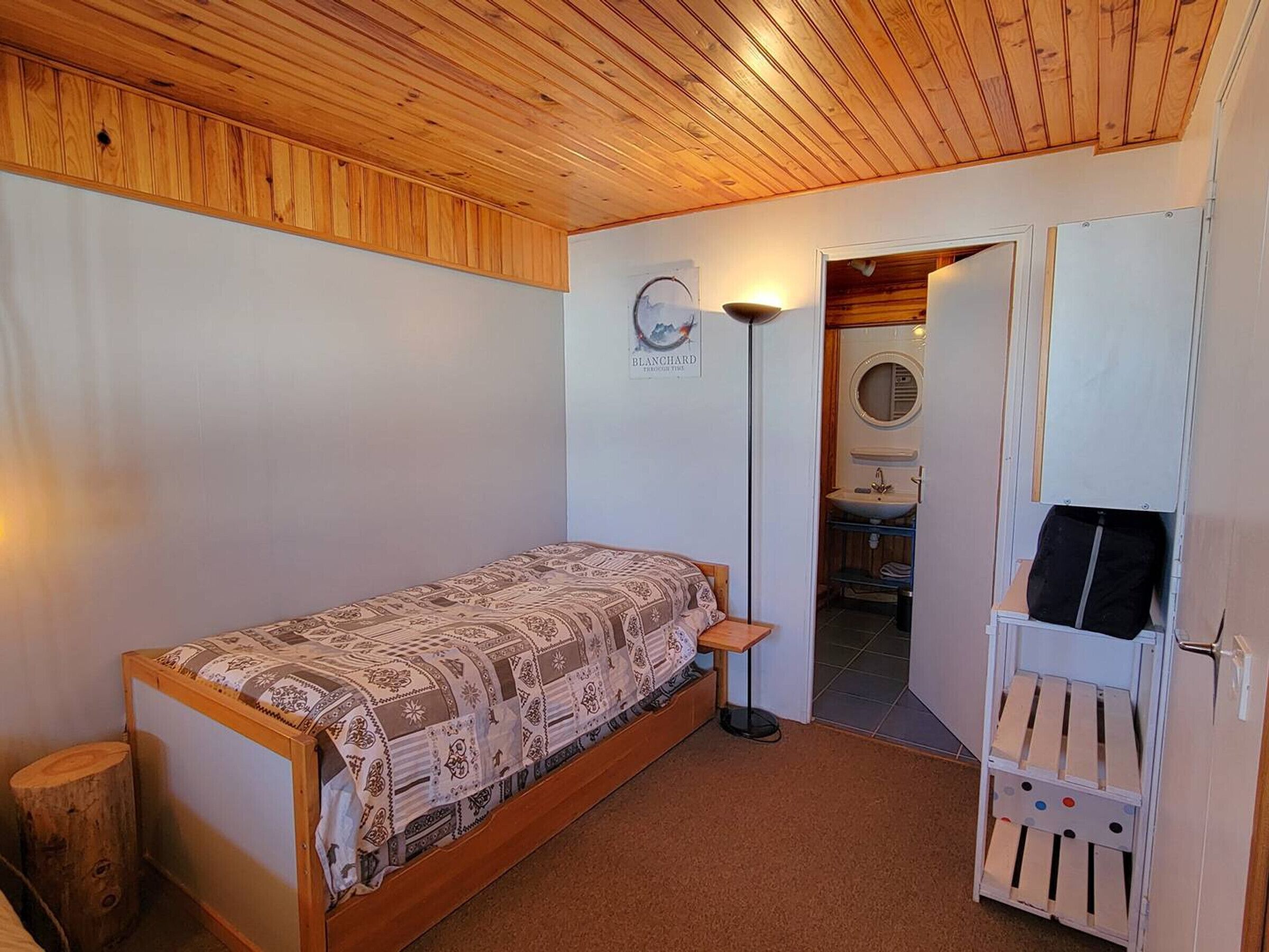 A small, cozy room with a single bed, a bedside table, a lamp, and a door leading to a bathroom.