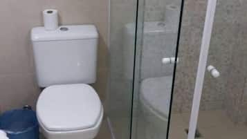 A bathroom with a toilet, a glass shower enclosure, and a blue trash bin.