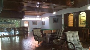 A billiards room with a pool table, several wicker chairs, and a bar area with stools.