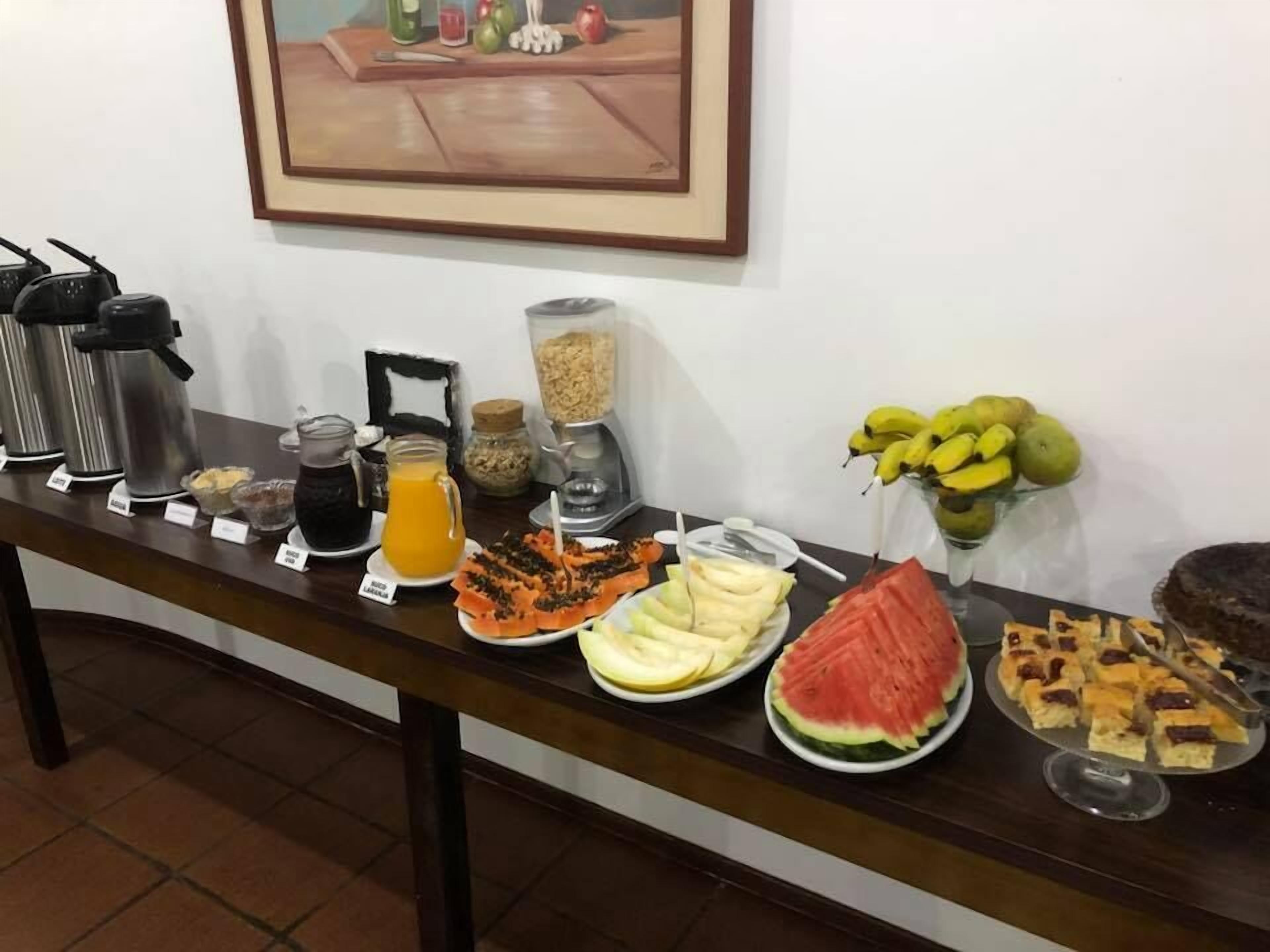 Une table de buffet proposant une variété d’aliments et de boissons, notamment des fruits, des sandwichs et un distributeur de jus.