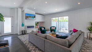 Una sala de estar moderna con un sofá modular, dos sillones, una mesa de centro y un televisor montado en la pared.