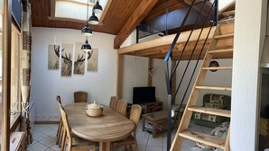 A dining area with a wooden table and chairs, a television, and a staircase leading to an upper level.