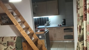 A cozy kitchen with a wooden staircase, a dining table, and a sofa.