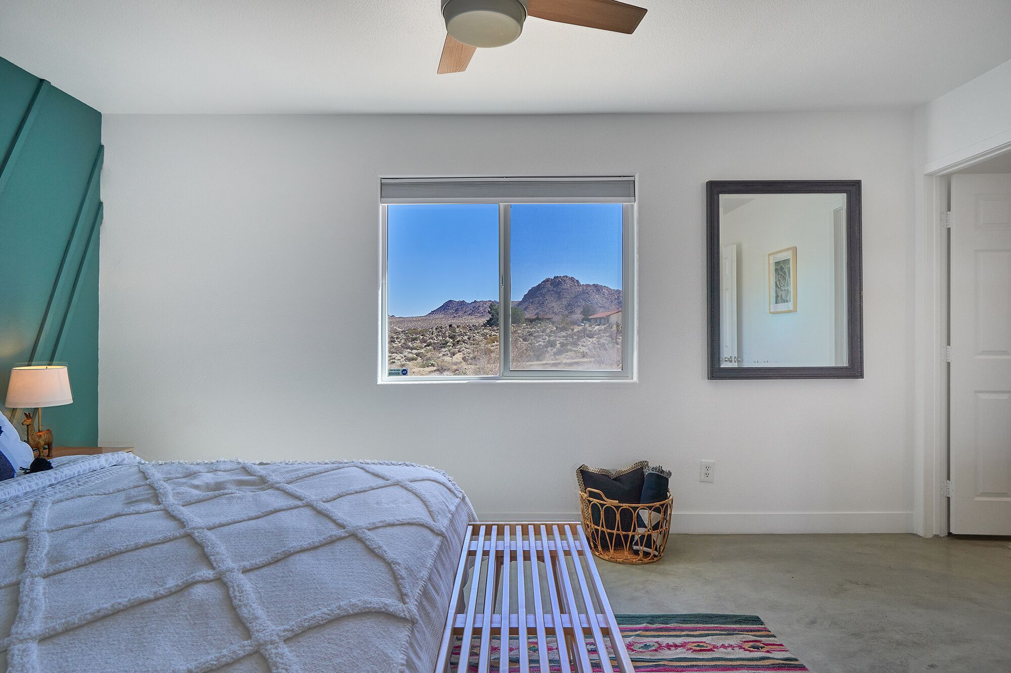 A bedroom with a bed, a window with a view of mountains, a ceiling fan, and a wall-mounted mirror.