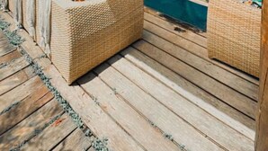 A wooden deck with wicker furniture and a glass door leading to a room. - Pousada Portal dos Golfinhos (Fernando de Noronha)