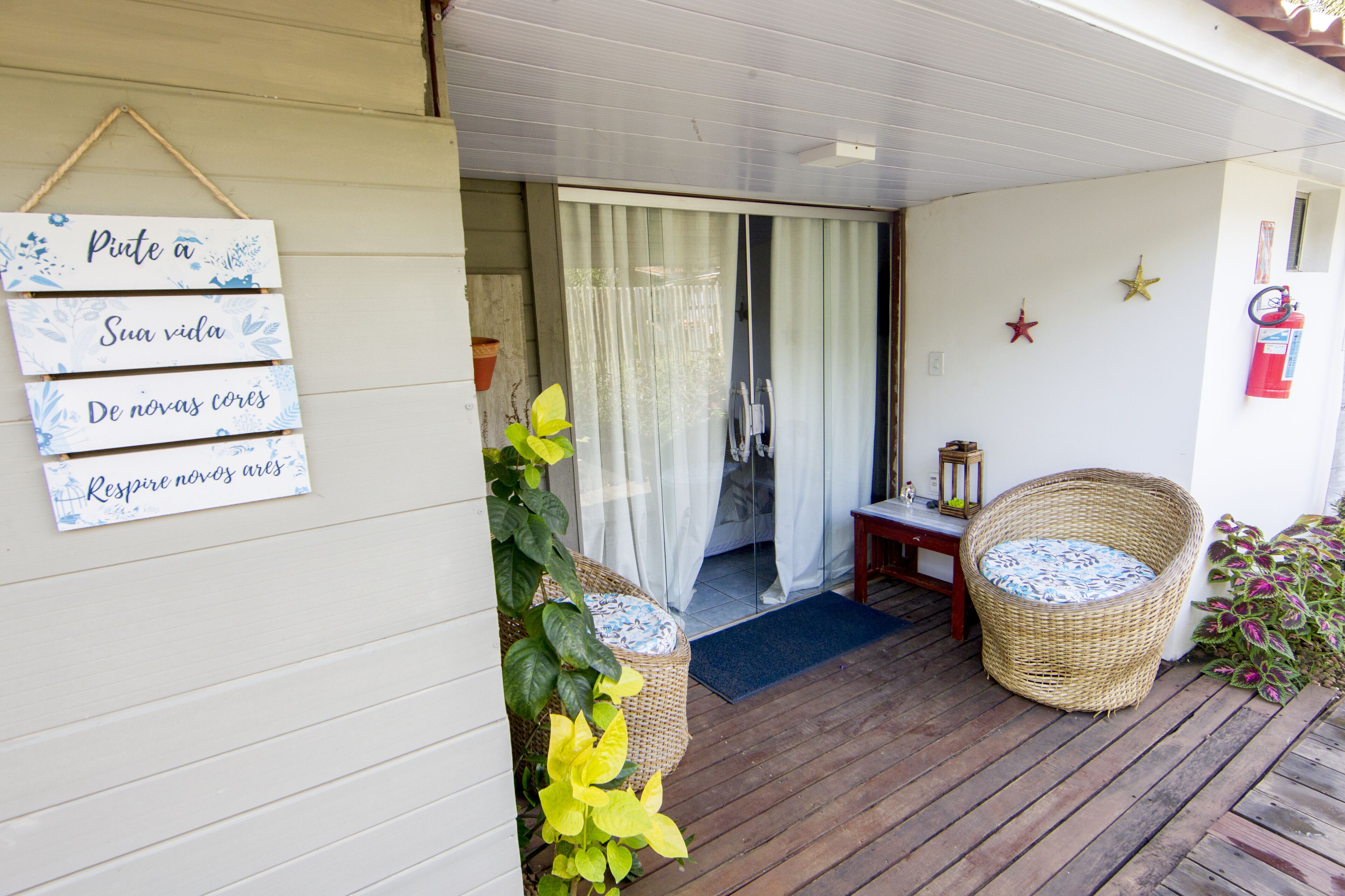 A wooden deck with wicker furniture, a sign with text, and a door with curtains.