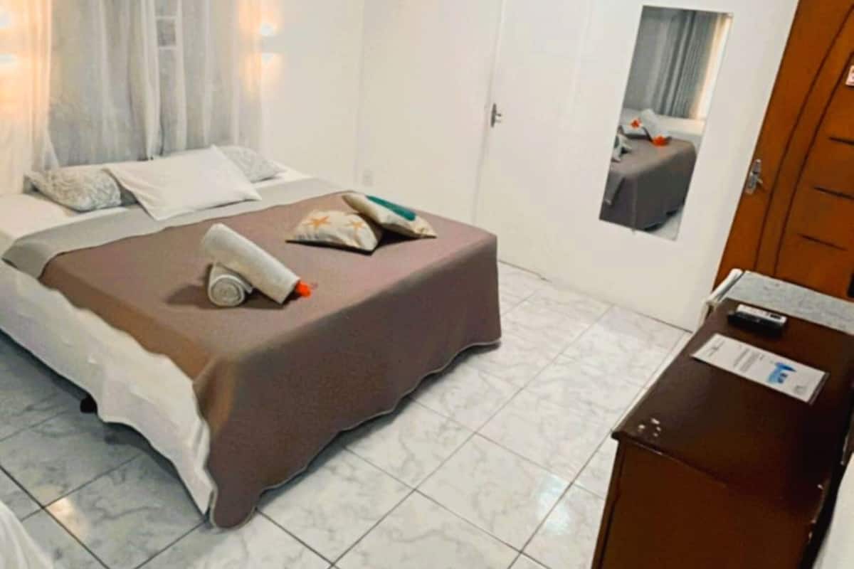 A hotel room with a bed, a desk, a chair, a door, and a window.