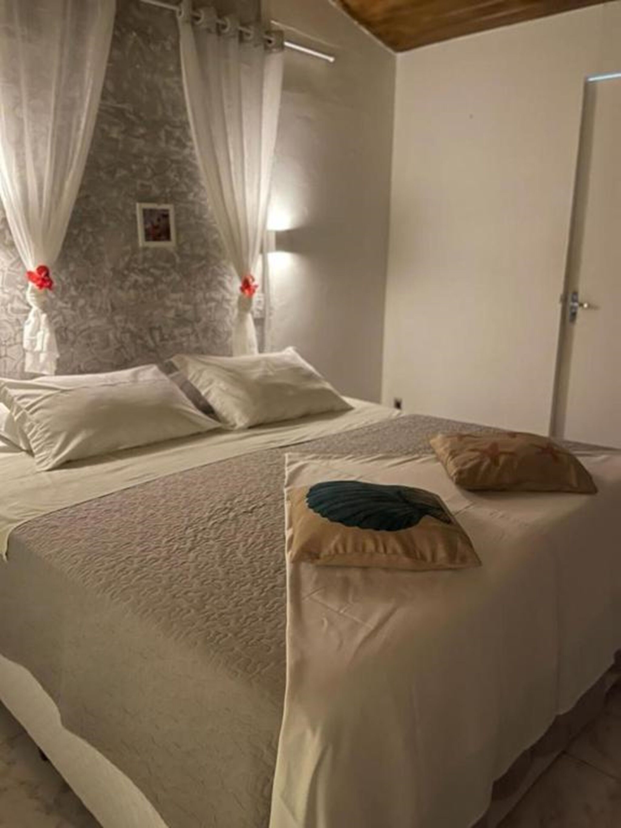 Ein Schlafzimmer mit einem Bett, weißen Vorhängen, einer Steinwand und einer Tür.